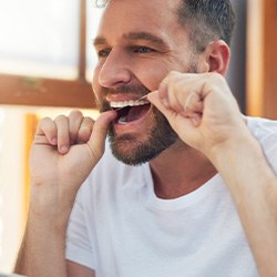 Man smiling while flossing his teeth in bathroom