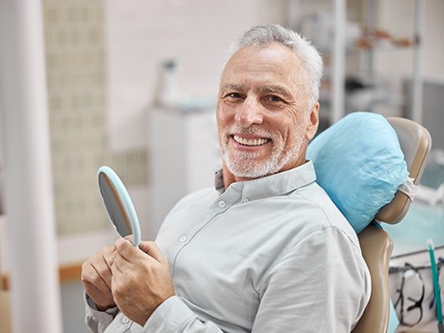 man smiling while holding dental mirror