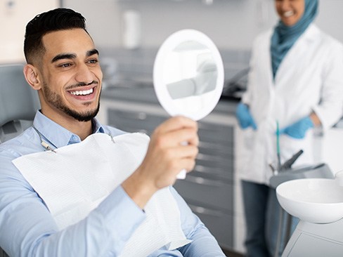 Man smiling while looking at reflection in handheld mirror