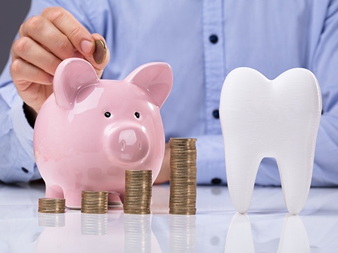 A large model tooth next to a man putting coins in a piggy bank