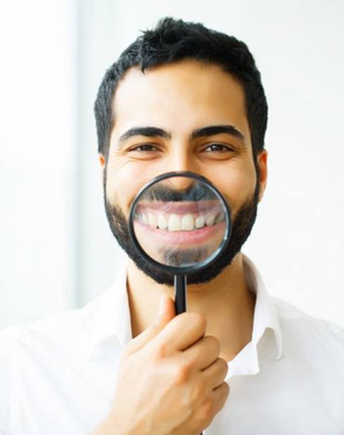 man with veneers in Garland holding a magnifying glass to his smile 
