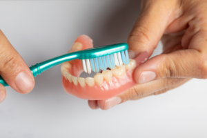 Close up of hands brushing a set of dentures